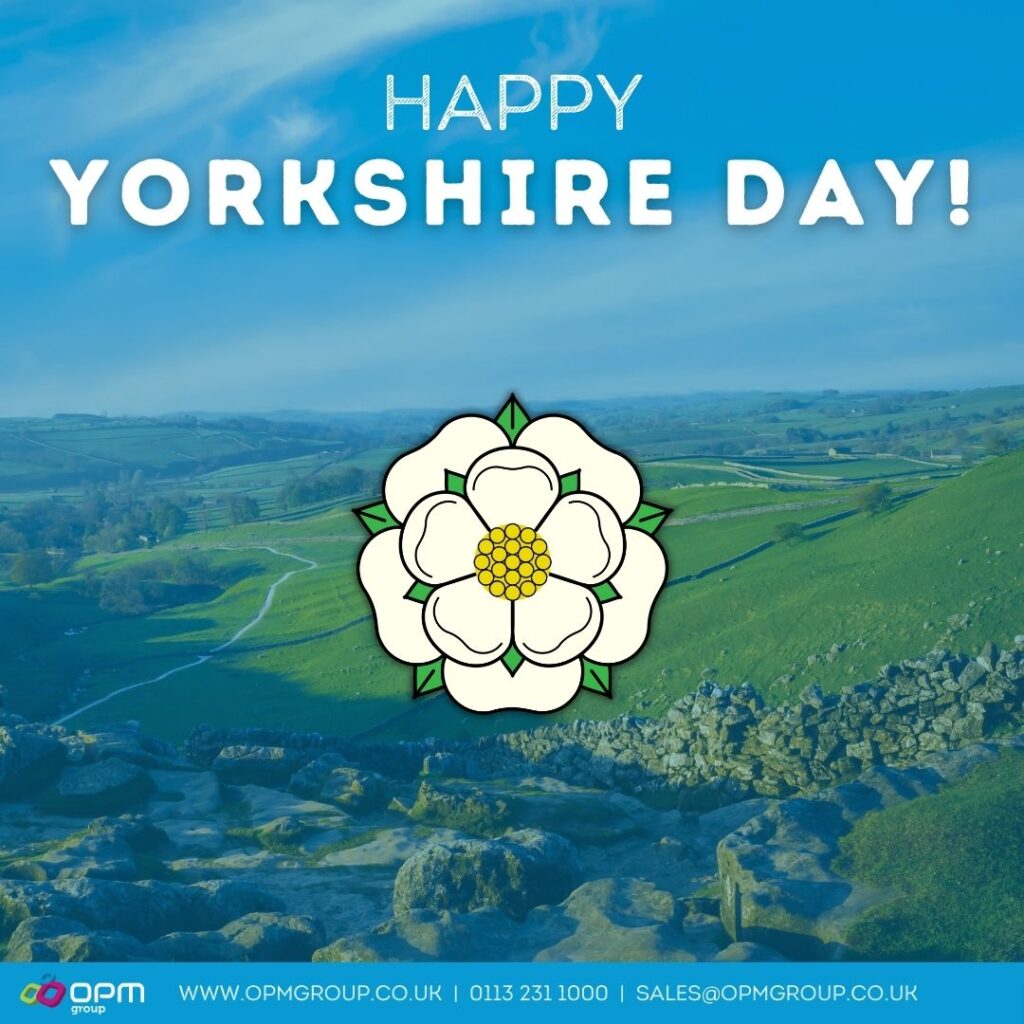 The background shows a rural Yorkshire countryside on a sunny day.It has a blue tint over the background image.There is white text at the top of the images which says 'Happy Yorkshire Day!'.The Yorkshire rose is in the middle of the square.At the bottom, there is a blue strip which has the OPM Group logo in the bottom left corner, followed by OPM Group's contact details. Telephone - 0113 231 1000E-mail. - sales@opmgroup.co.uk Website - www.opmgroup.co.uk